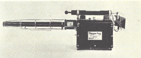 Yellowed black and white photo of a stationary pepper fog thermal fogger pointed to the left sitting by itself. The main body is a square box that's dark with a tag in the middle that's lighter and has dark writing on it that says pepper fog g o e c. The nozzle points to the left and is a longer thinner tube about twice as long as the main body. It is also dark and has a metal cage around it that is sparse and shiny. There's also a handle and some knobs on the top of the item and something that's a little bit difficult to make out off the back of the main body.